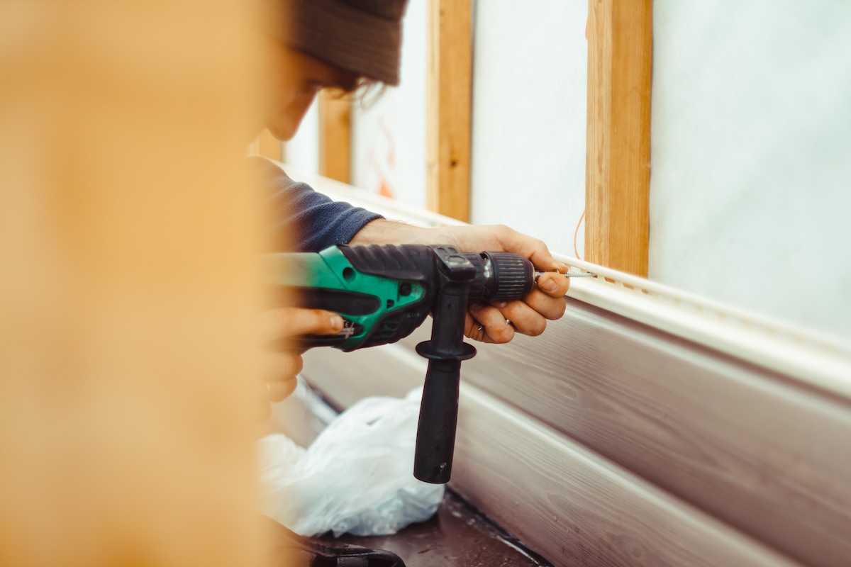 A worker installs panels beige siding on the facade of the house