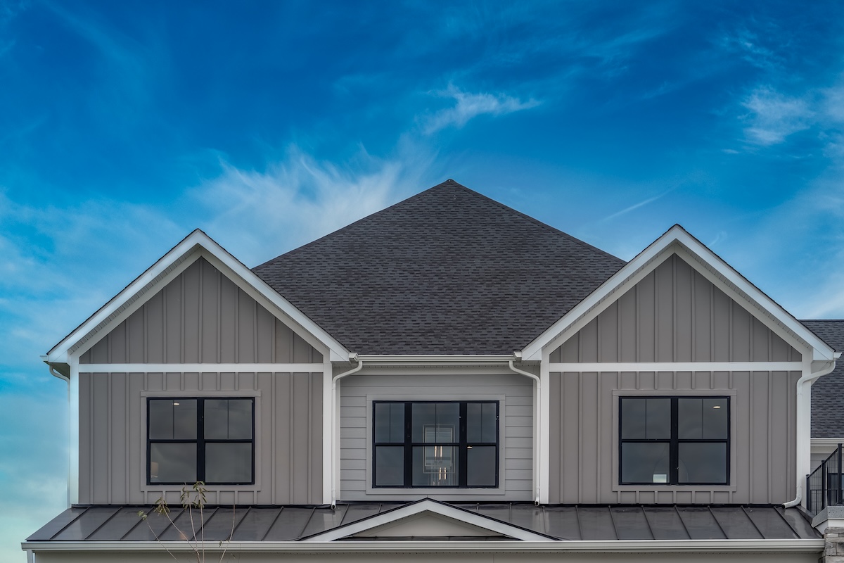 Upscale American house façade with vertical beige vinyl siding white accents, black framed aluminum windows metal roof cover over the porch, double gable roof with dreamy blue sky in the USA