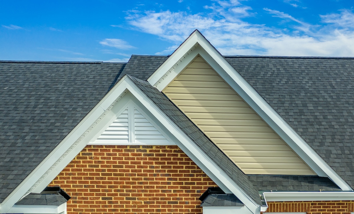 siding materials Double gable with beige horizontal vinyl lap and red brick facade siding, with triangle shape white attic vent on a pitched roof attic at an American single family home neighborhood USA