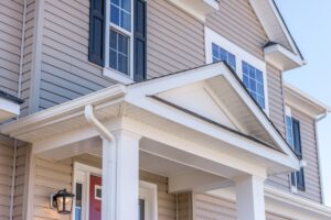 Portico leading to the entrance of vinyl horizontal lap siding covered building, with a roof structure over a walkway, supported by white rectangular columns on a new single family home in Maryland lap siding
