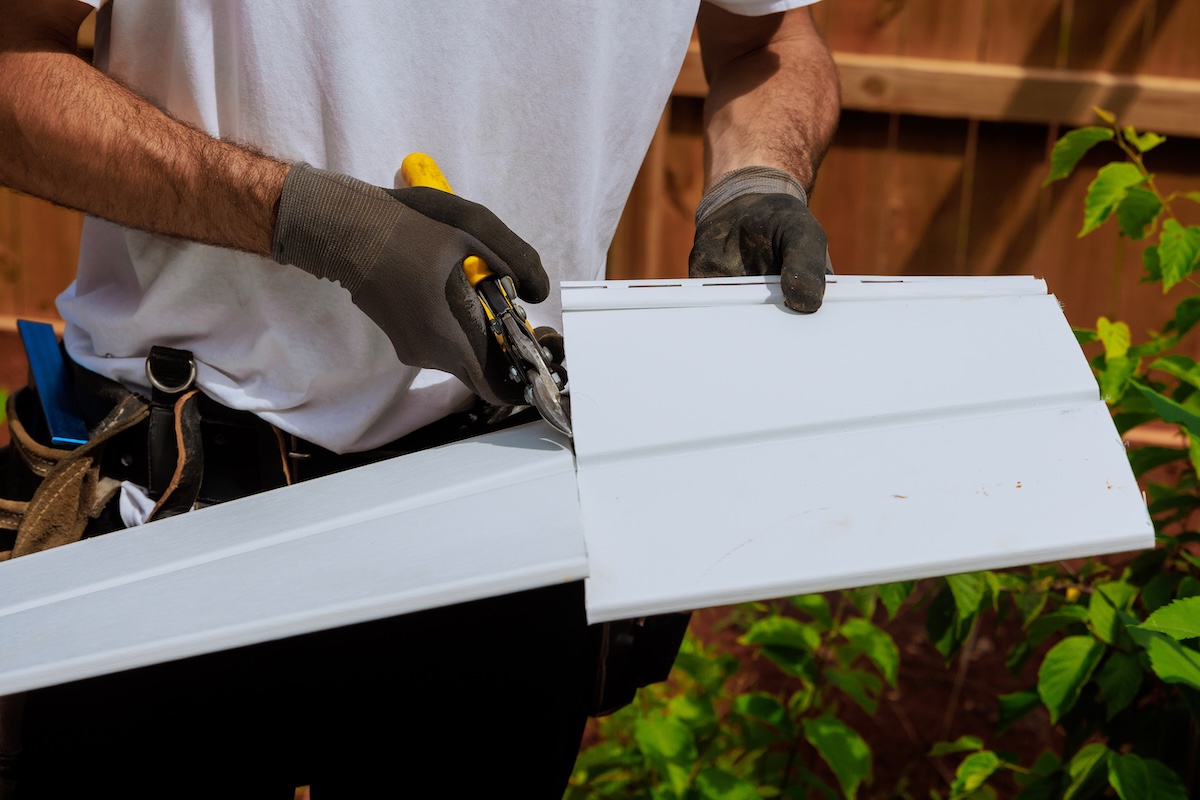 Worker cuts plastic vinyl siding to size before it is installed using scissors