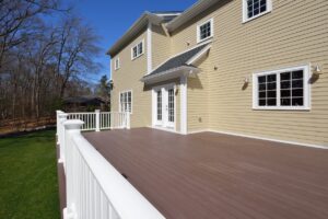 Large new deck in house backyard. Composite boards, white railing posts and veranda