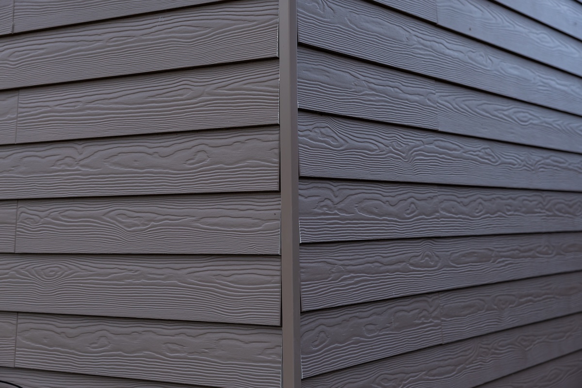 engineered wood siding The corner of a house features gray horizontal siding with a wood grain texture, emphasizing clean lines and modern architectural design.