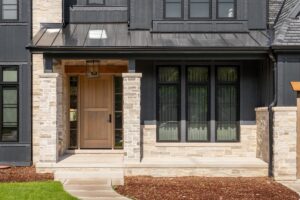 A front door detail on a home with black board and batten siding with natural stone accents and a beautiful oak front door.