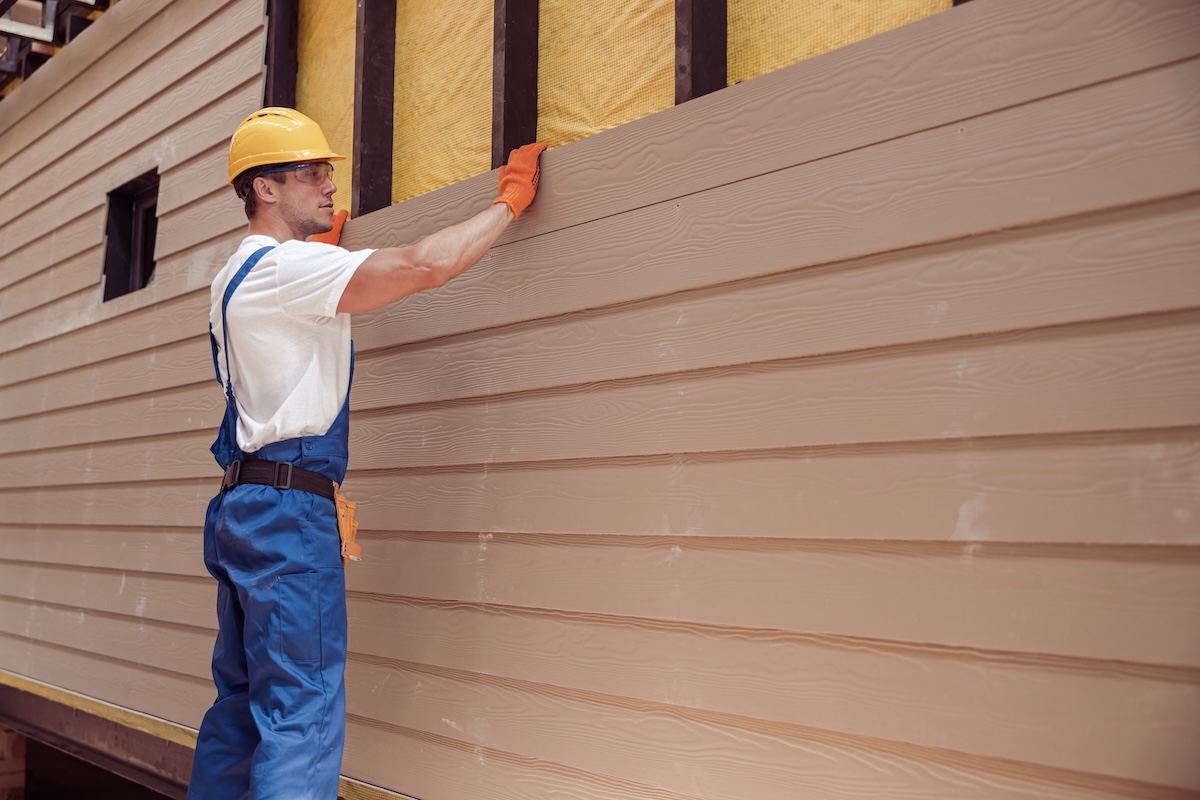 engineered wood siding Handsome young man construction worker wearing safety helmet and work overalls while installing wood siding