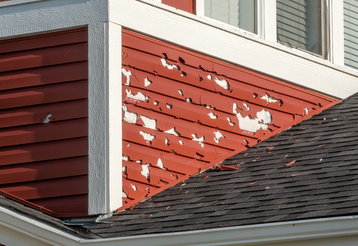 A close-up of a building's exterior shows red siding with extensive hail damage, exposing the underlying white surface. hail damage siding