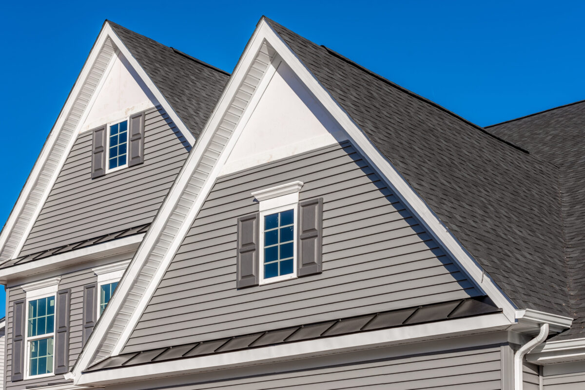 house siding options Double gable, with white decorative trim over the windows on a triangle gable roof, white soffit and fascia,  gray horizontal vinyl lap siding with blue sky background